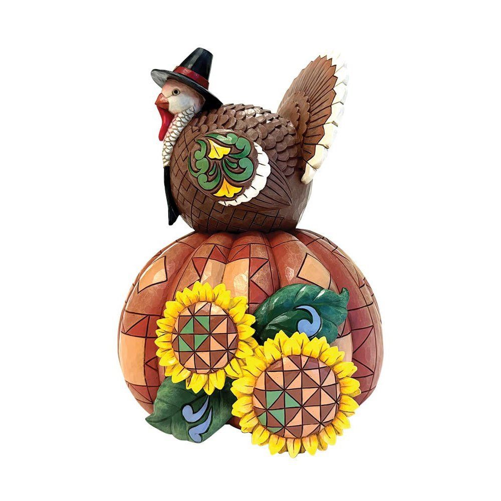 Een kalkoenfiguurtje met een pelgrimshoed op, bovenop een pompoen versierd met zonnebloemen.