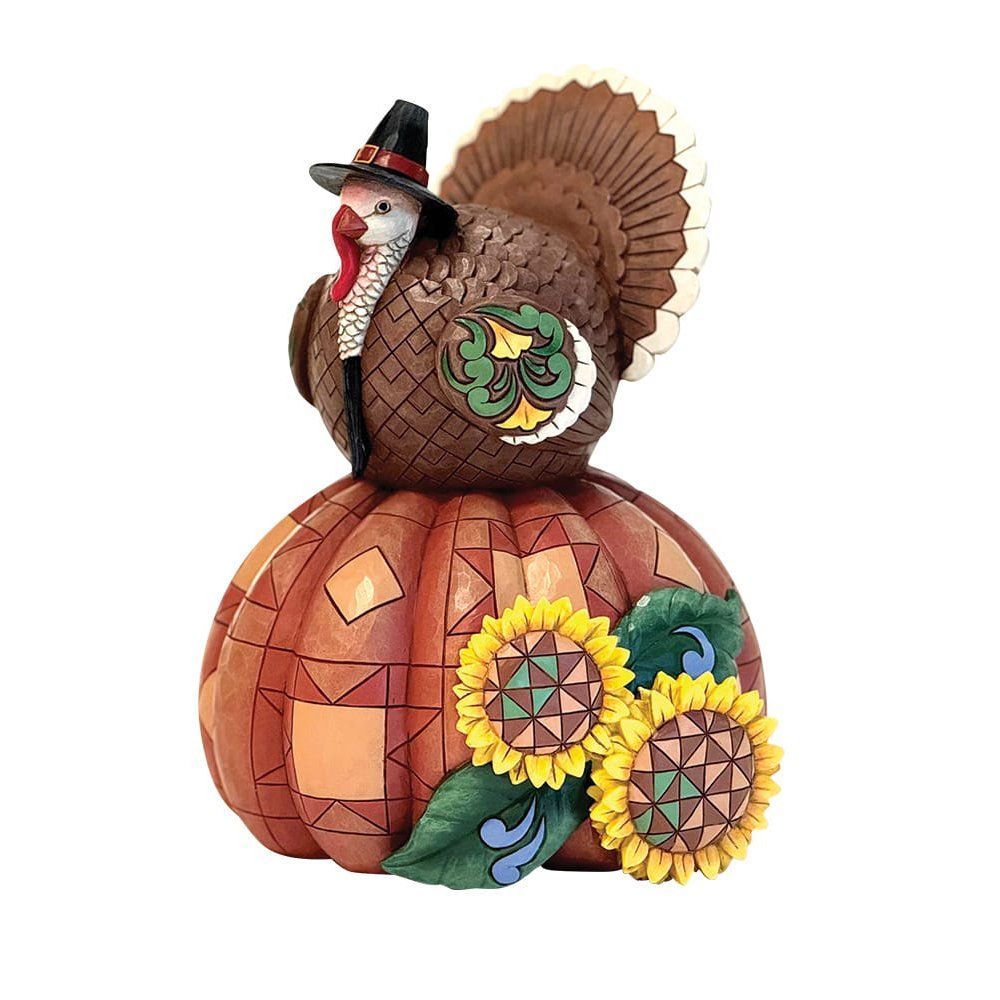 Een kalkoenfiguurtje met een pelgrimshoed op, bovenop een pompoen versierd met zonnebloemen.