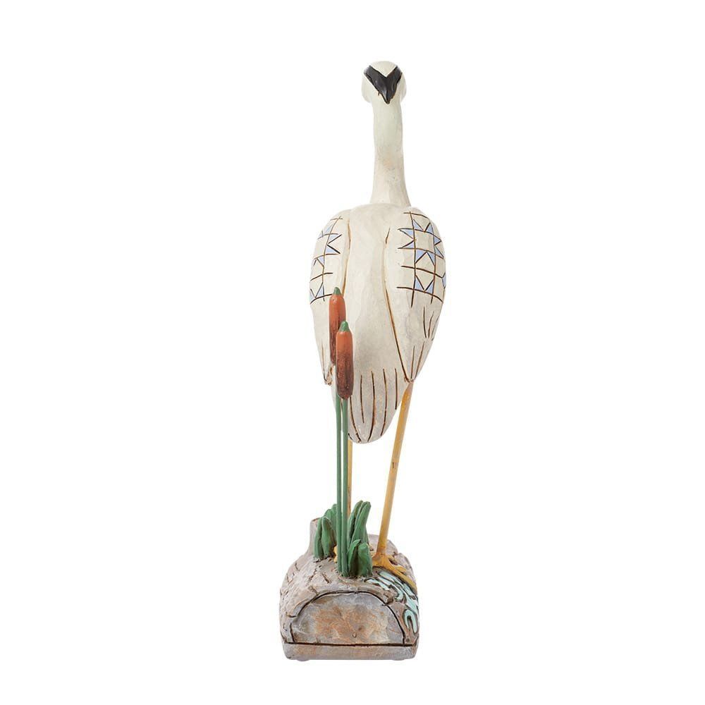 Een uit hout gesneden beeld van een witte reiger met gedetailleerde tekeningen, staand op een gestructureerde sokkel met lisdodden.