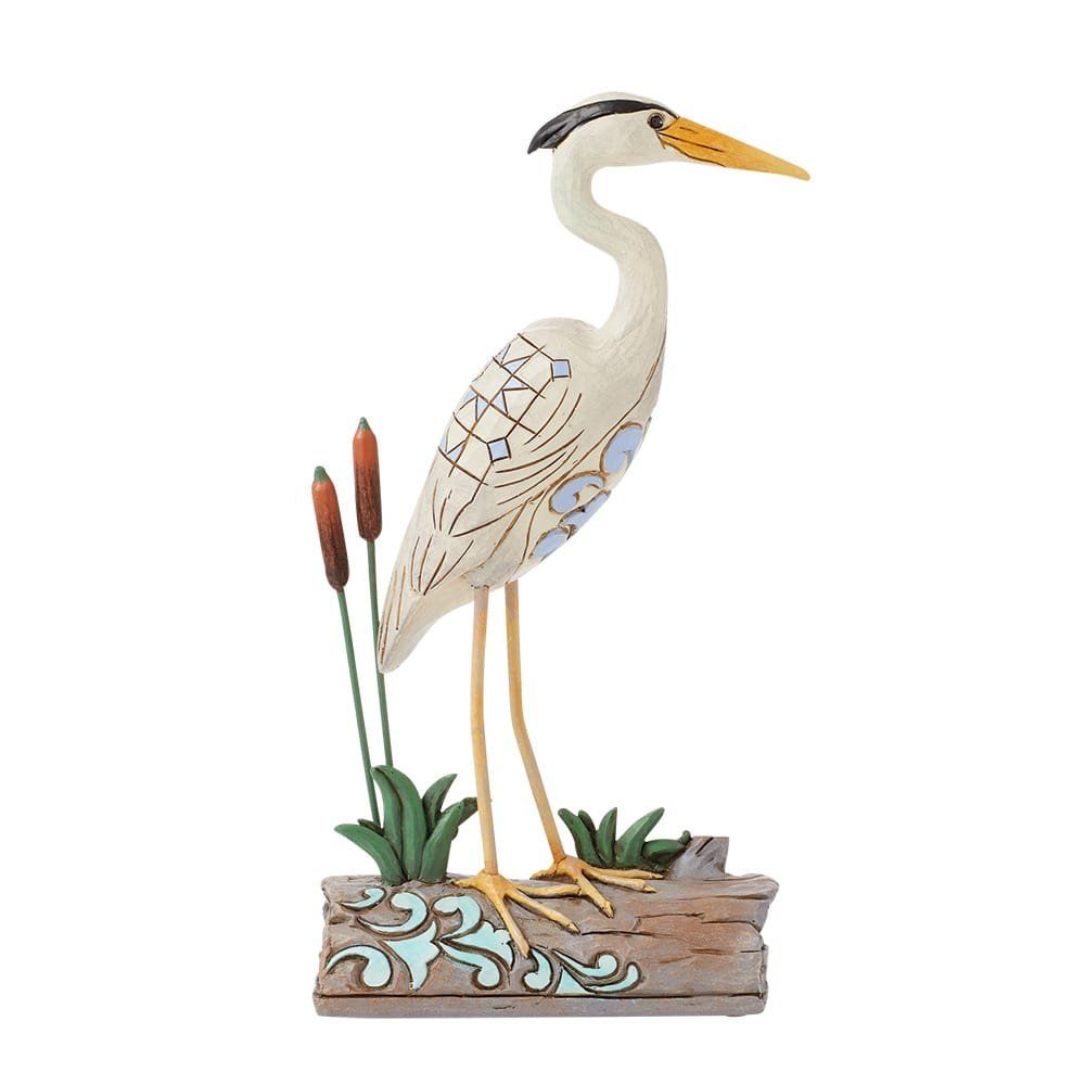 Standbeeld van een reiger, crèmekleurig lichaam, zwarte kopmarkeringen, staand op een boomstam met riet.