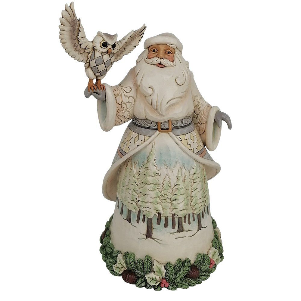 Een kerstmanfiguur met een uil in zijn armen, gekleed in een witte mantel met een boslandschap op de rok, zittend op een bed van groen gebladerte.