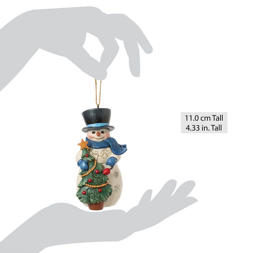 Een sneeuwpopfiguur die een kerstboom vasthoudt, een blauwe sjaal en hoge hoed draagt en een beige lijfje heeft.