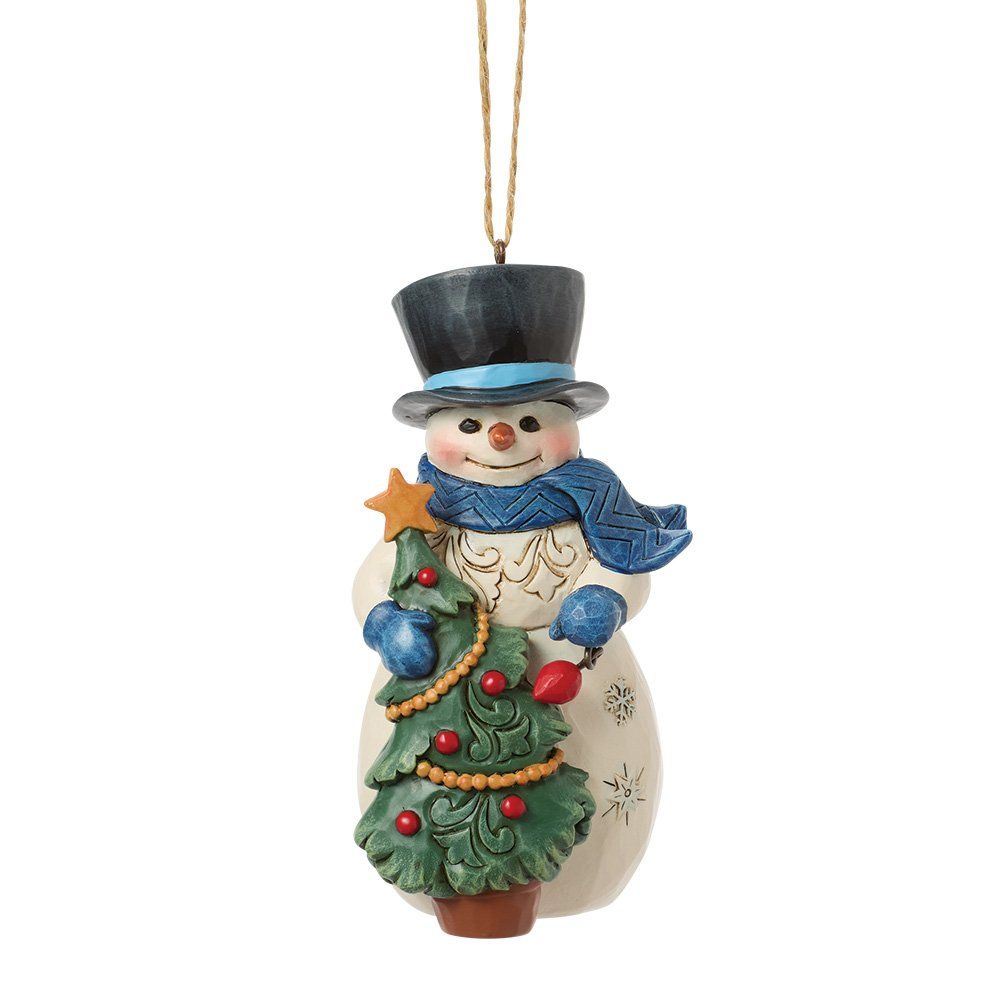 Een sneeuwpopfiguur die een kerstboom vasthoudt, een blauwe sjaal en hoge hoed draagt en een beige lijfje heeft.
