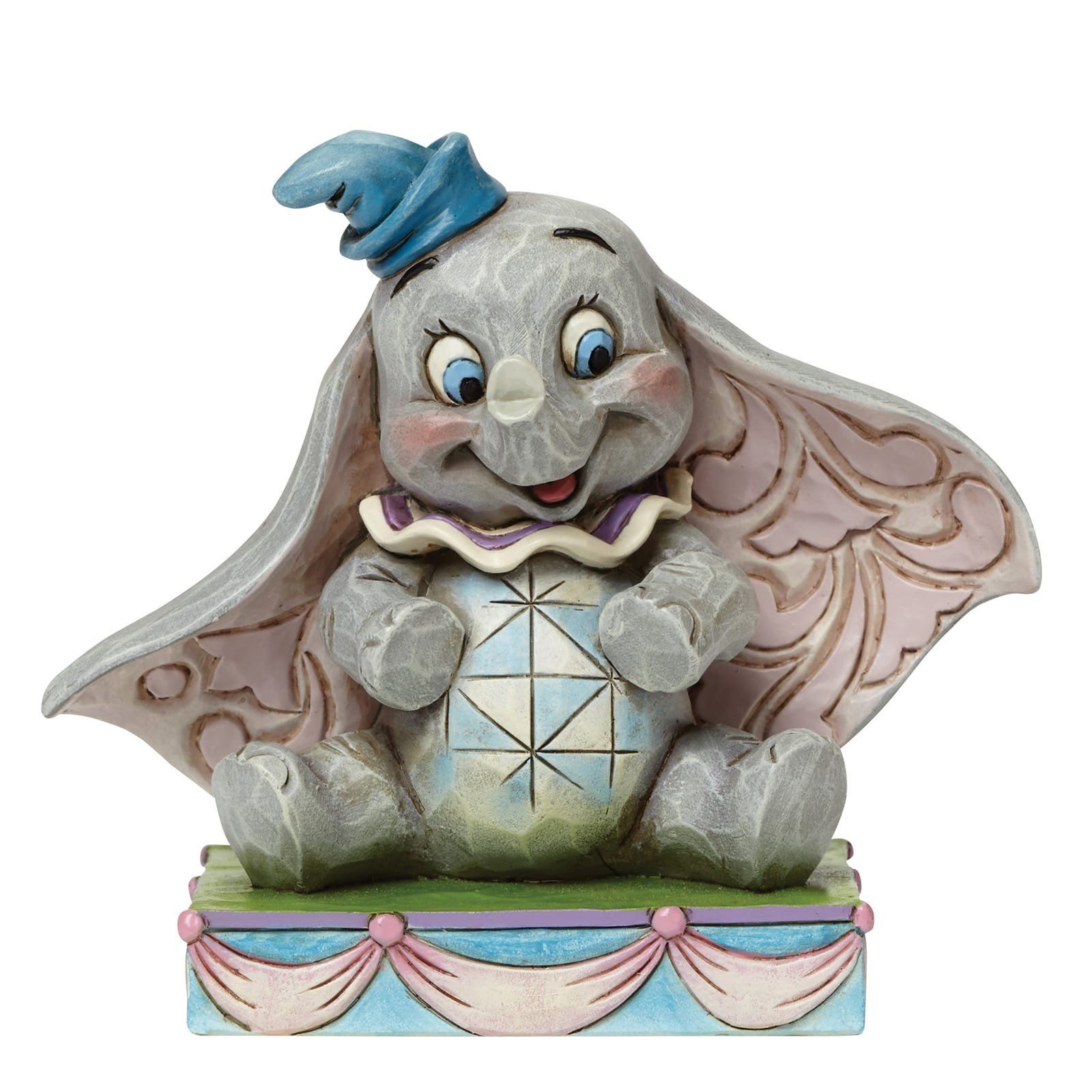 Een Dumbo-figuurtje met grote oren en een blauwe hoed, lachend, zittend op een versierde sokkel.