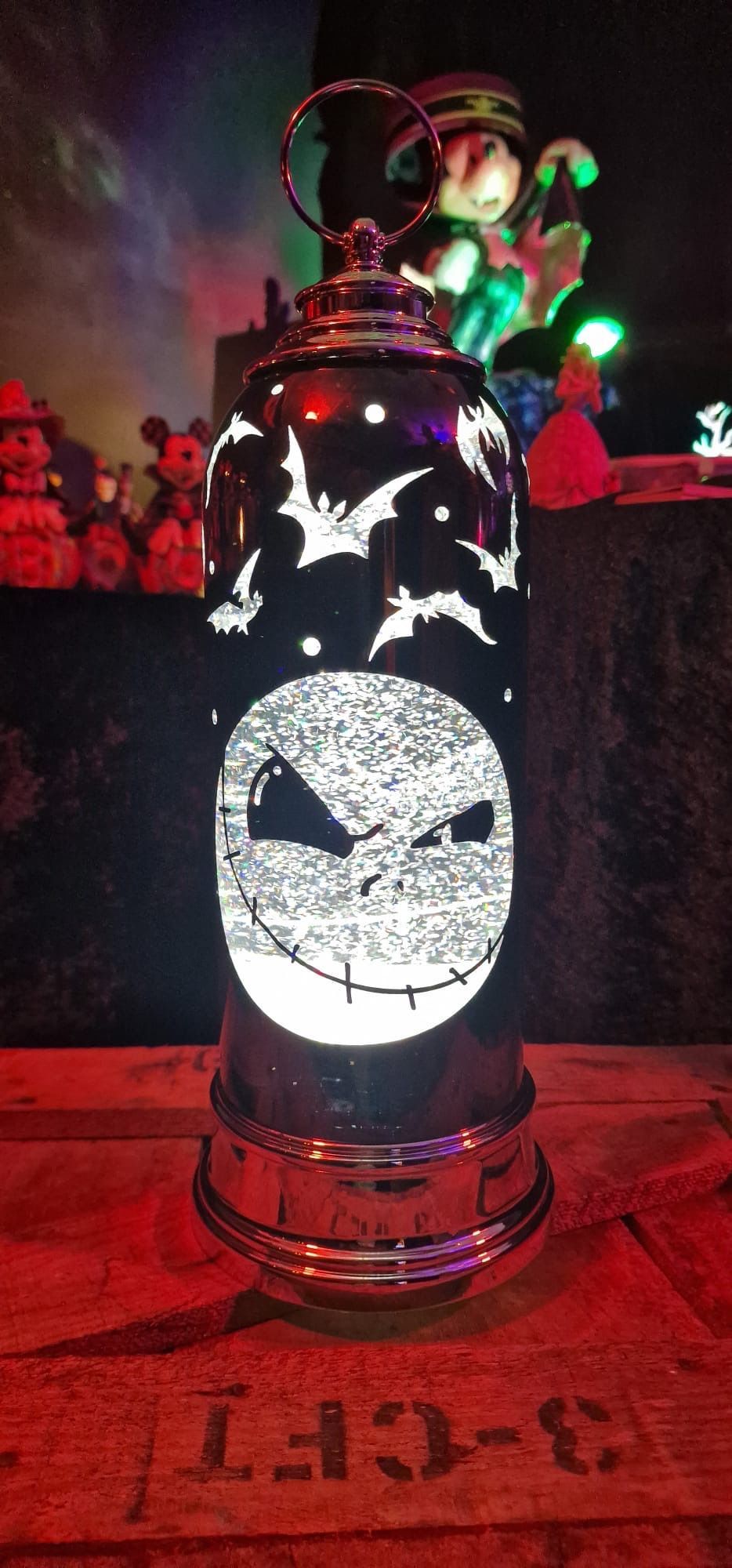 Een lantaarn met Jack Skellington-thema, versierd met vleermuizen en sterren, staat op een houten ondergrond.