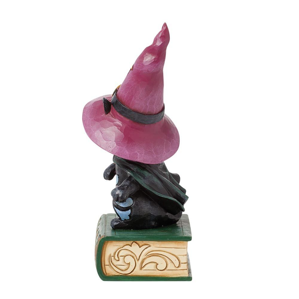 Een klein zwart figuurtje met een paarse heksenhoed en cape, die een boek leest.