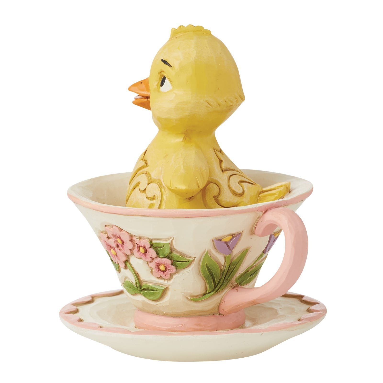 Een geel kuikentje zit in een theekopje met bloemenprint.