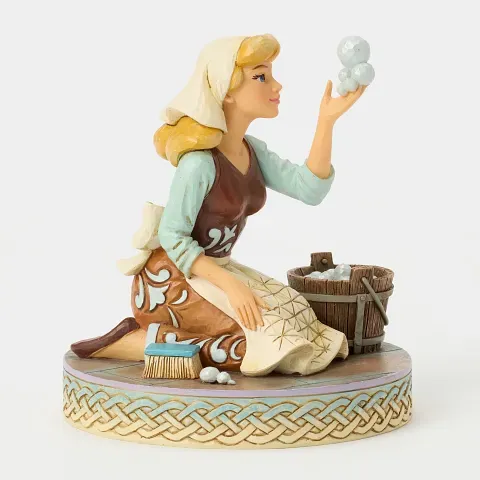 Een Assepoester-beeldje, knielend naast een emmer, die de zeepbellen bewondert. Lichtblauw, bruin en blond haar.
