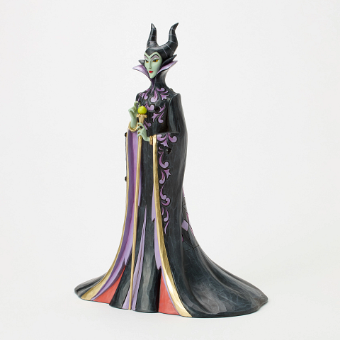 Een beeldje van Maleficent, met een groene bol in haar hand, gekleed in zwarte en paarse gewaden en met hoorns, tegen een witte achtergrond.