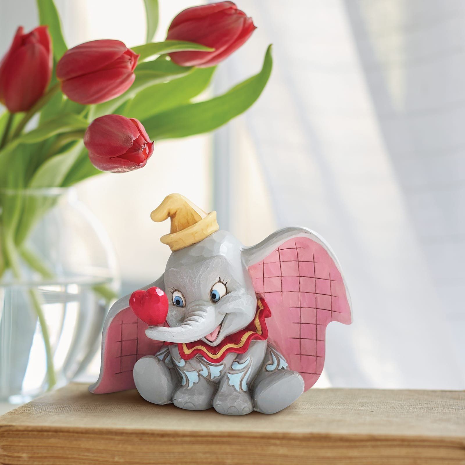 Een Dumbo-figuurtje met een rood hartje, zittend op een boek met tulpen op de achtergrond.