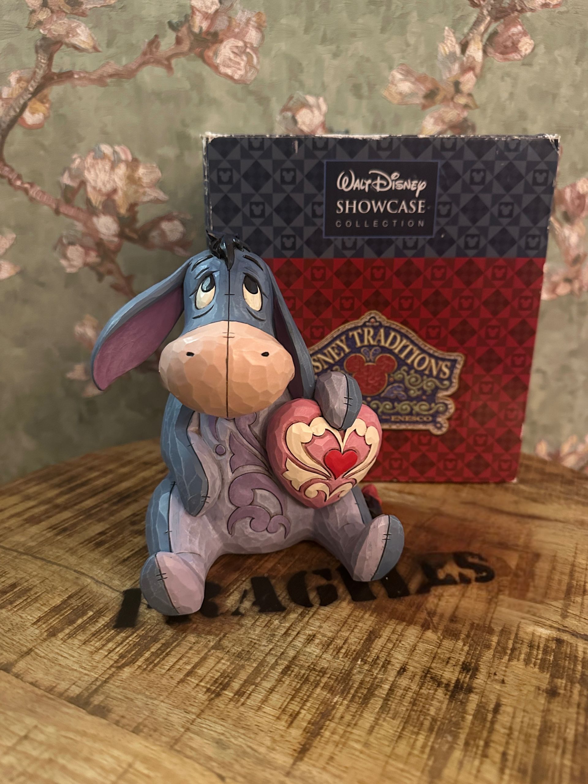 Een beeldje van Eeyore met een hart in zijn hand, met op de achtergrond een doos van Disney Traditions.