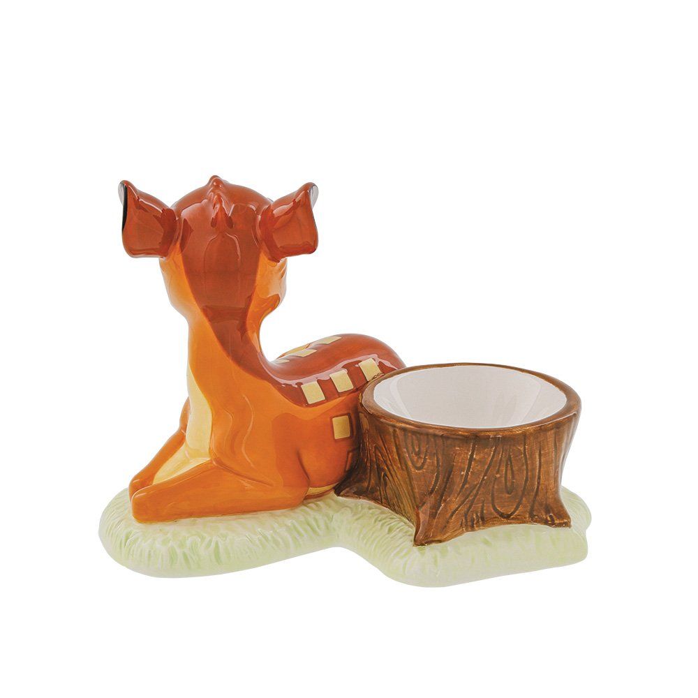 Een Bambi-beeldje, een oranje hertje liggend in het gras, naast een bruine, uitgeholde boomstronk.