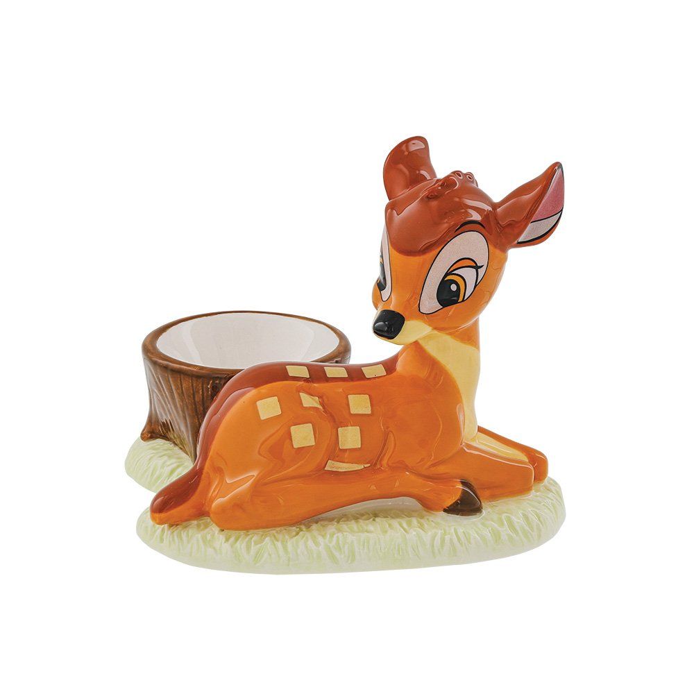 Een Bambi-beeldje, een oranje hertje liggend in het gras, naast een bruine, uitgeholde boomstronk.
