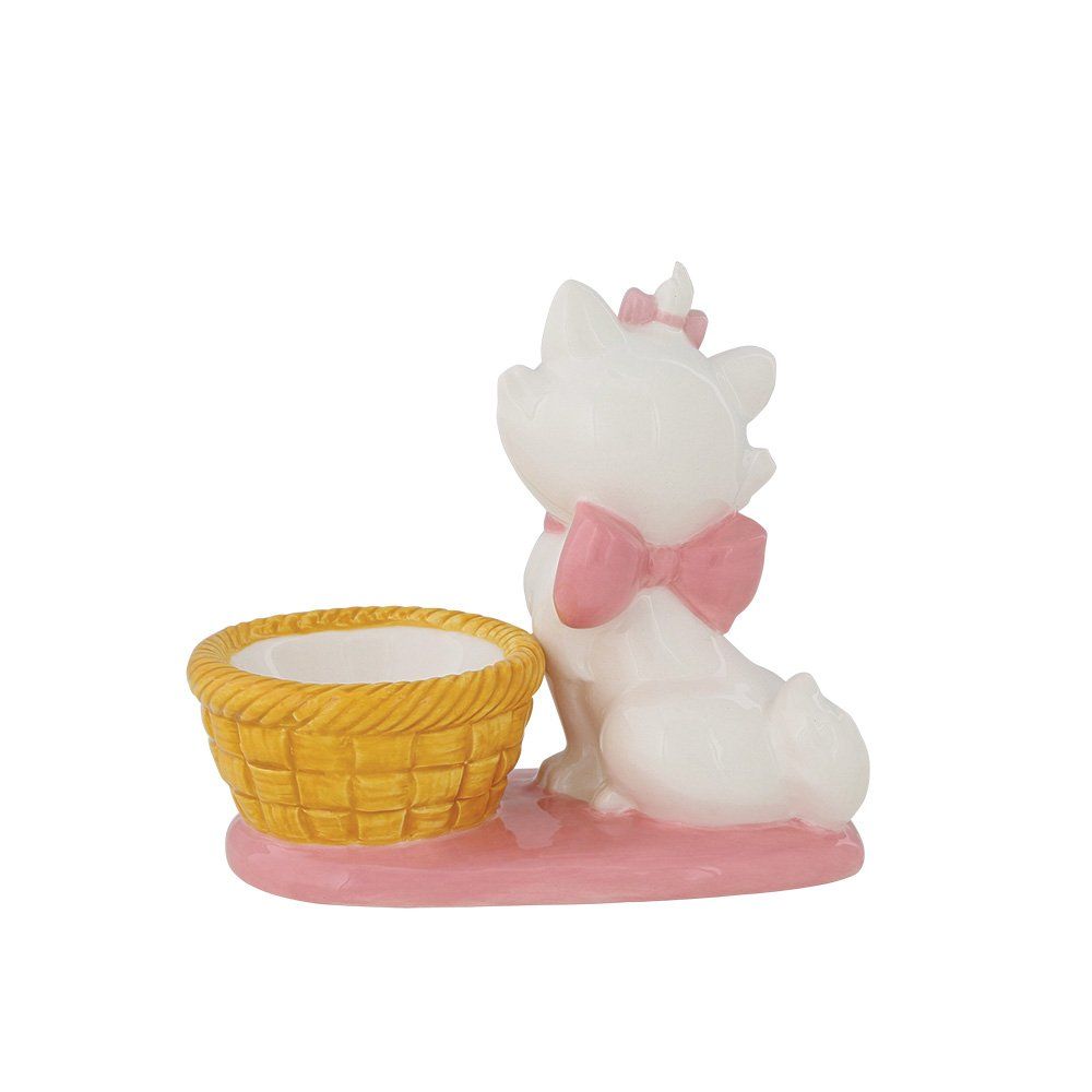 Het beeldje van kat Marie met een roze strik, zittend naast een geel gevlochten mandje, op een roze voetstuk.