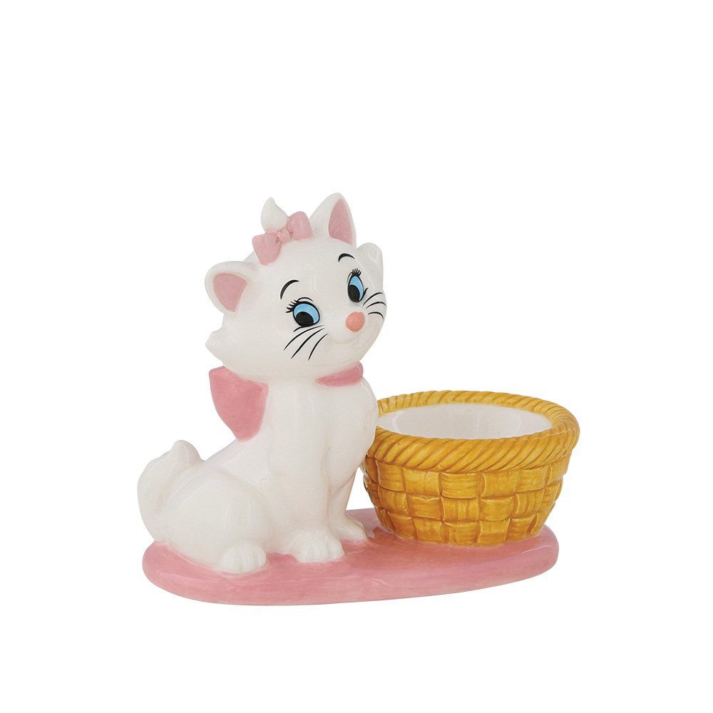 Het beeldje van kat Marie met een roze strik, zittend naast een geel gevlochten mandje, op een roze voetstuk.