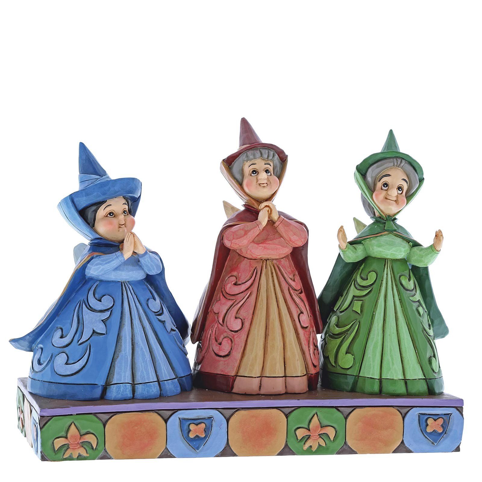 Drie gestileerde feeënfiguurtjes in blauwe, rode en groene jurken, op een decoratieve sokkel.