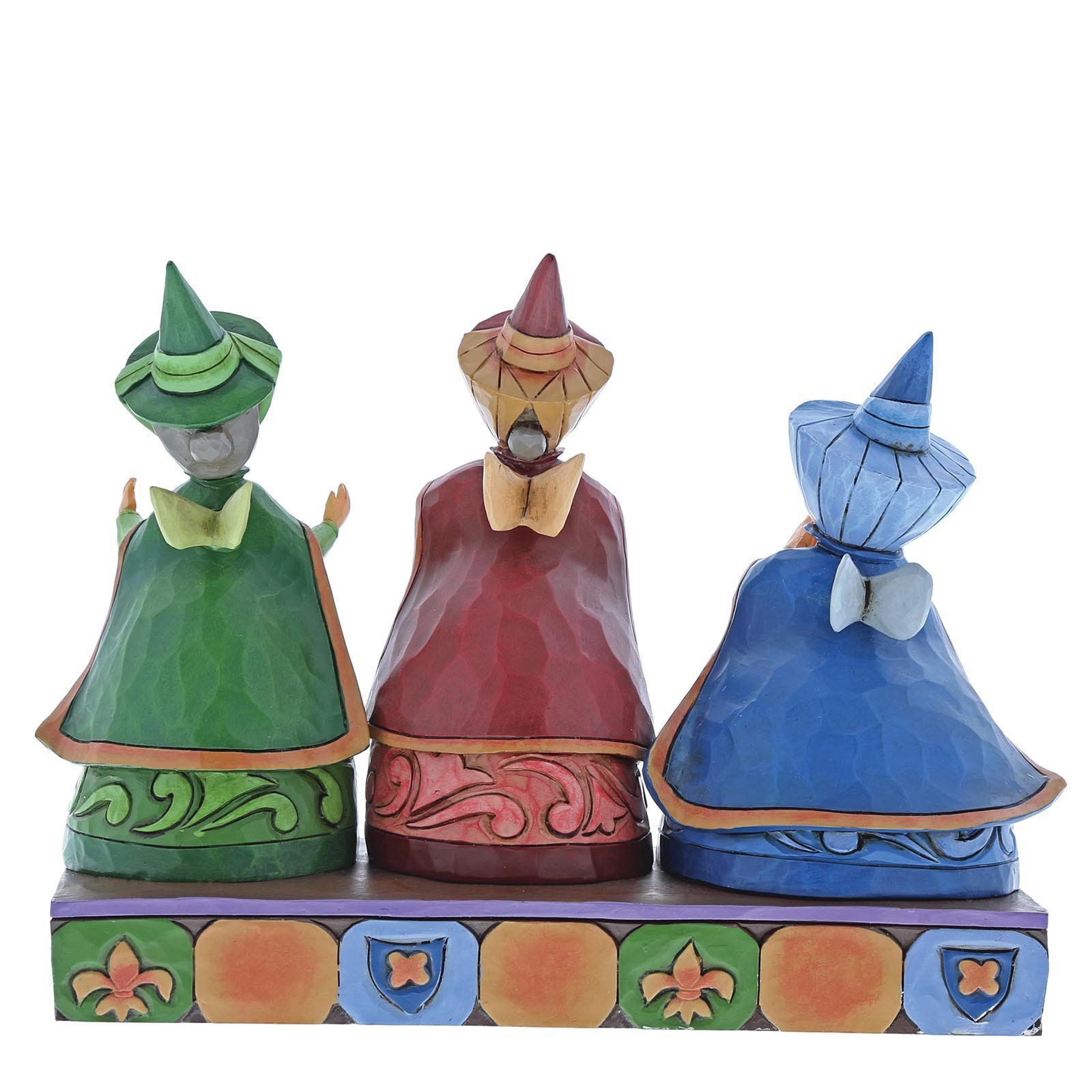Drie gebeeldhouwde figuren in groene, rode en blauwe gewaden, met heksenhoeden op, staan op een decoratieve sokkel.