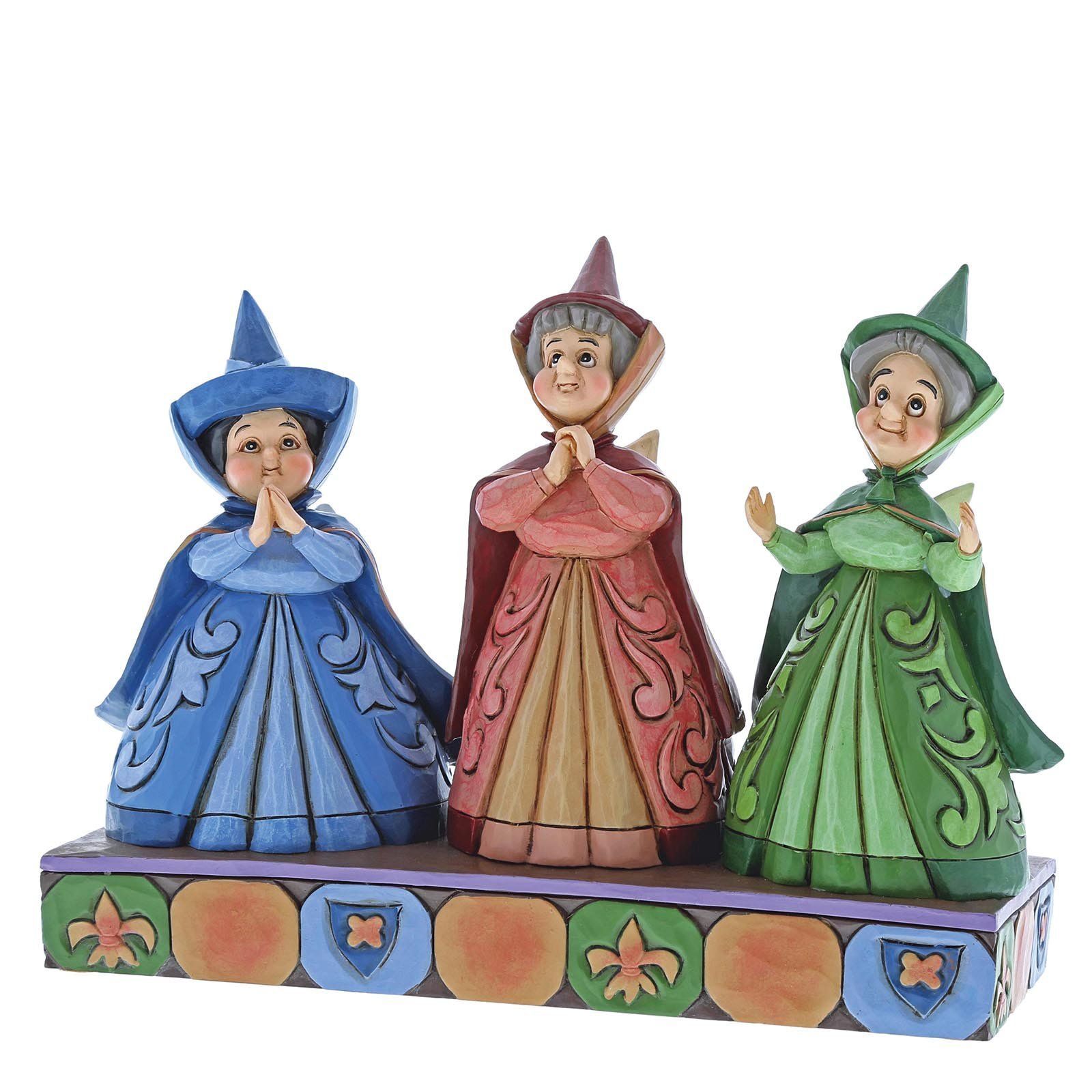 Drie gestileerde feeënfiguurtjes in blauwe, rode en groene jurken, op een decoratieve sokkel.