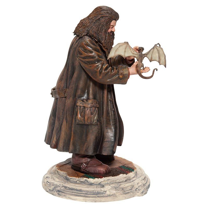 Standbeeld van Hagrid uit Harry Potter die een babydraak vasthoudt, op een rotsachtige sokkel.