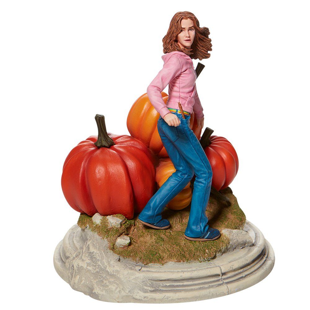 Standbeeld van Hermione Granger met pompoenen. Ze draagt een roze top en spijkerbroek en staat op een rotsachtige sokkel.