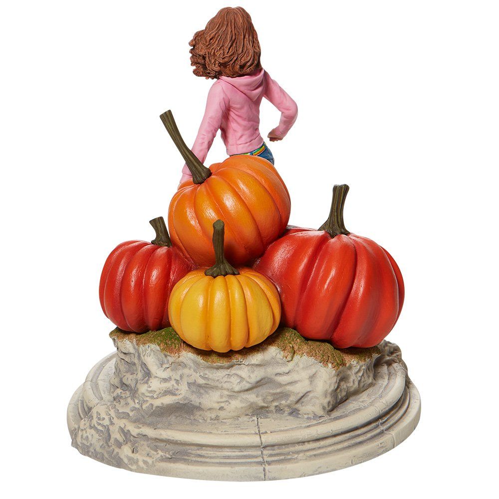 Standbeeld van Hermione Granger met pompoenen. Ze draagt een roze top en spijkerbroek en staat op een rotsachtige sokkel.