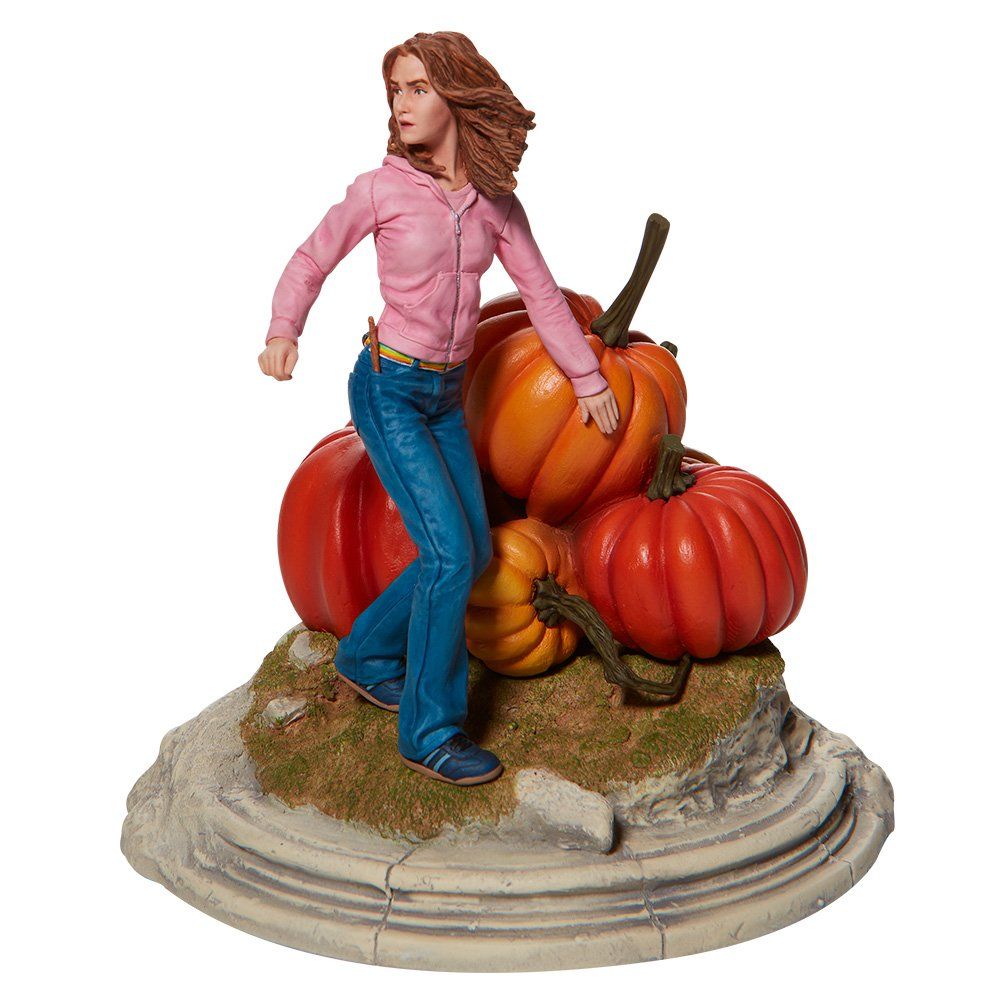 Een figuur van Hermione Granger, afgebeeld bovenop pompoenen, met een roze shirt en spijkerbroek aan. Op een stenen sokkel.