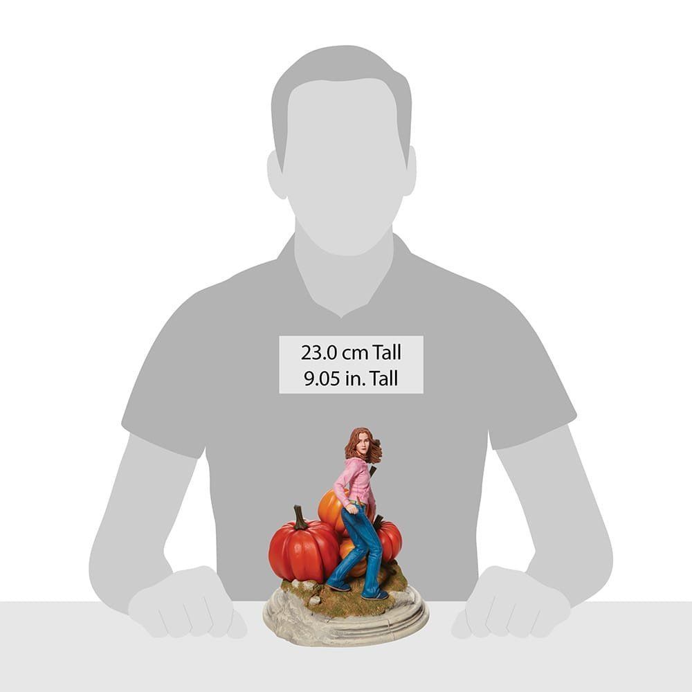 Figuurtje van een persoon in een blauwe spijkerbroek en een roze shirt naast pompoenen. 23 cm hoog.