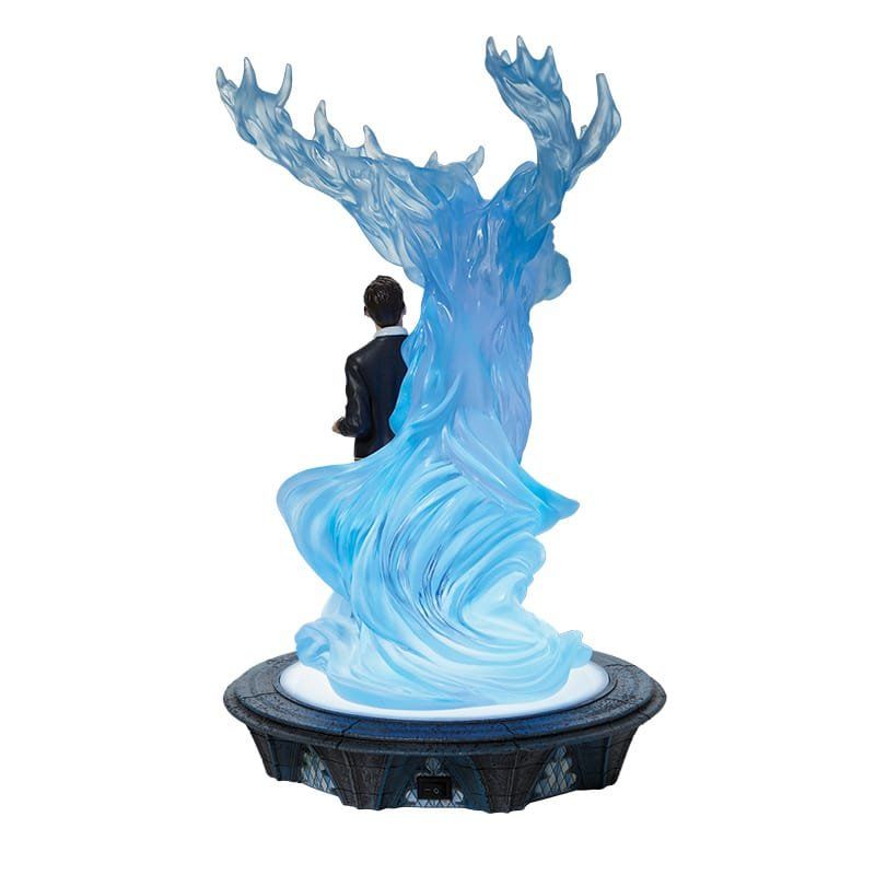Beeldje van een hert als Patronus, met blauw licht, dat een in een donker pak geklede figuur beschermt, op een decoratieve sokkel.