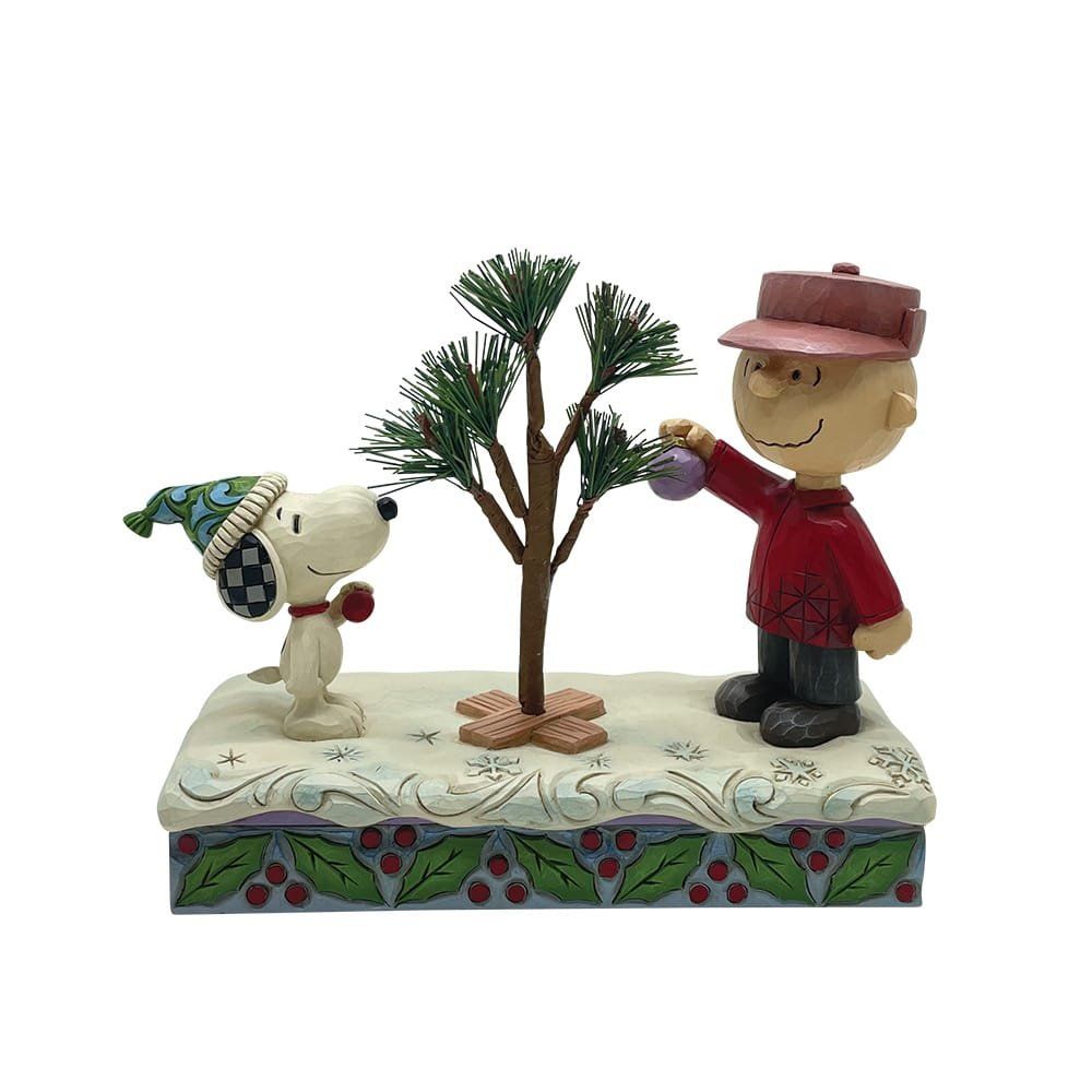 Snoopy en Charlie Brown versieren een kleine kerstboom. Snoopy draagt een hoed, Charlie Brown lacht.