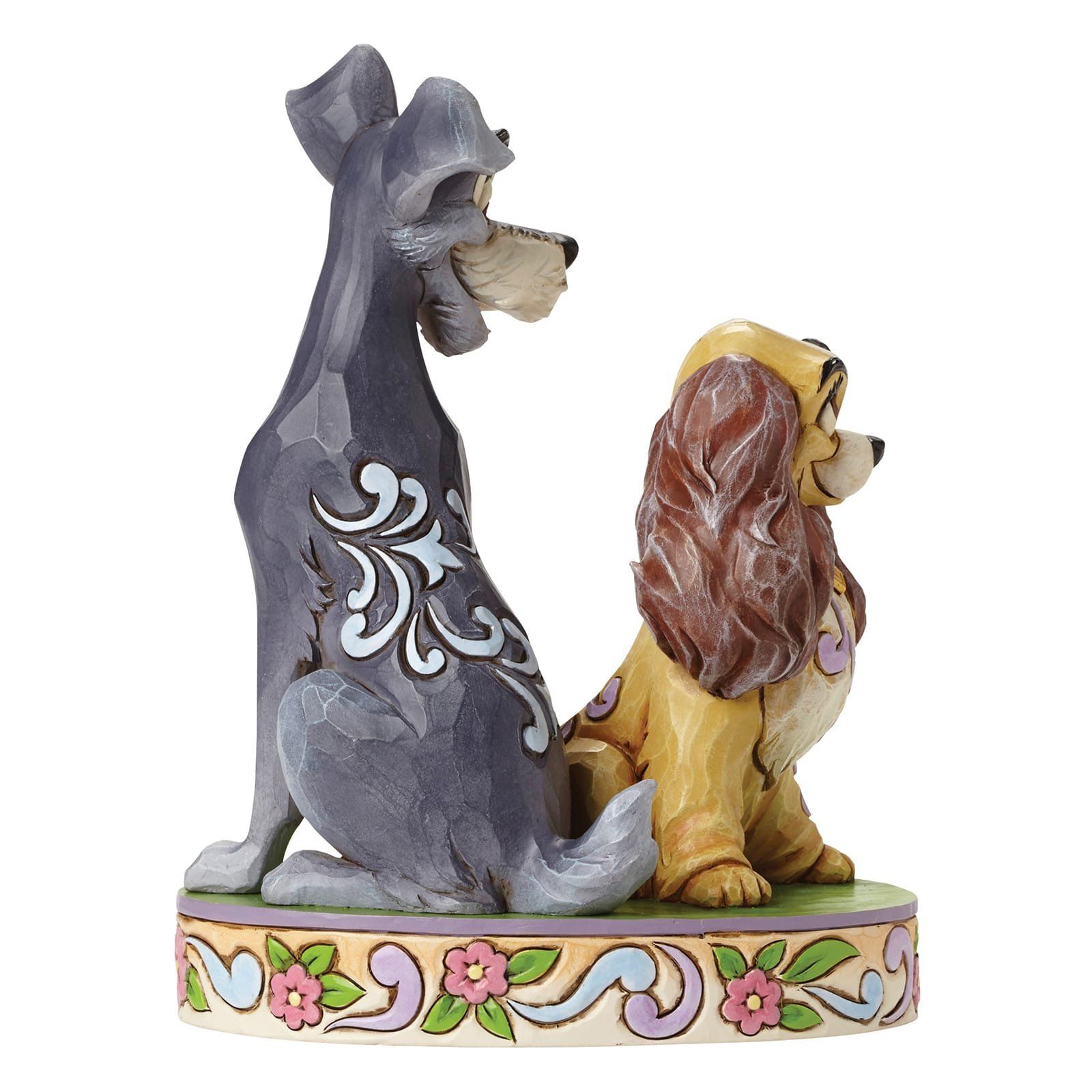 Beeldje van Lady en Tramp, een beige en een grijze hond, op een voetstuk met bloemen.
