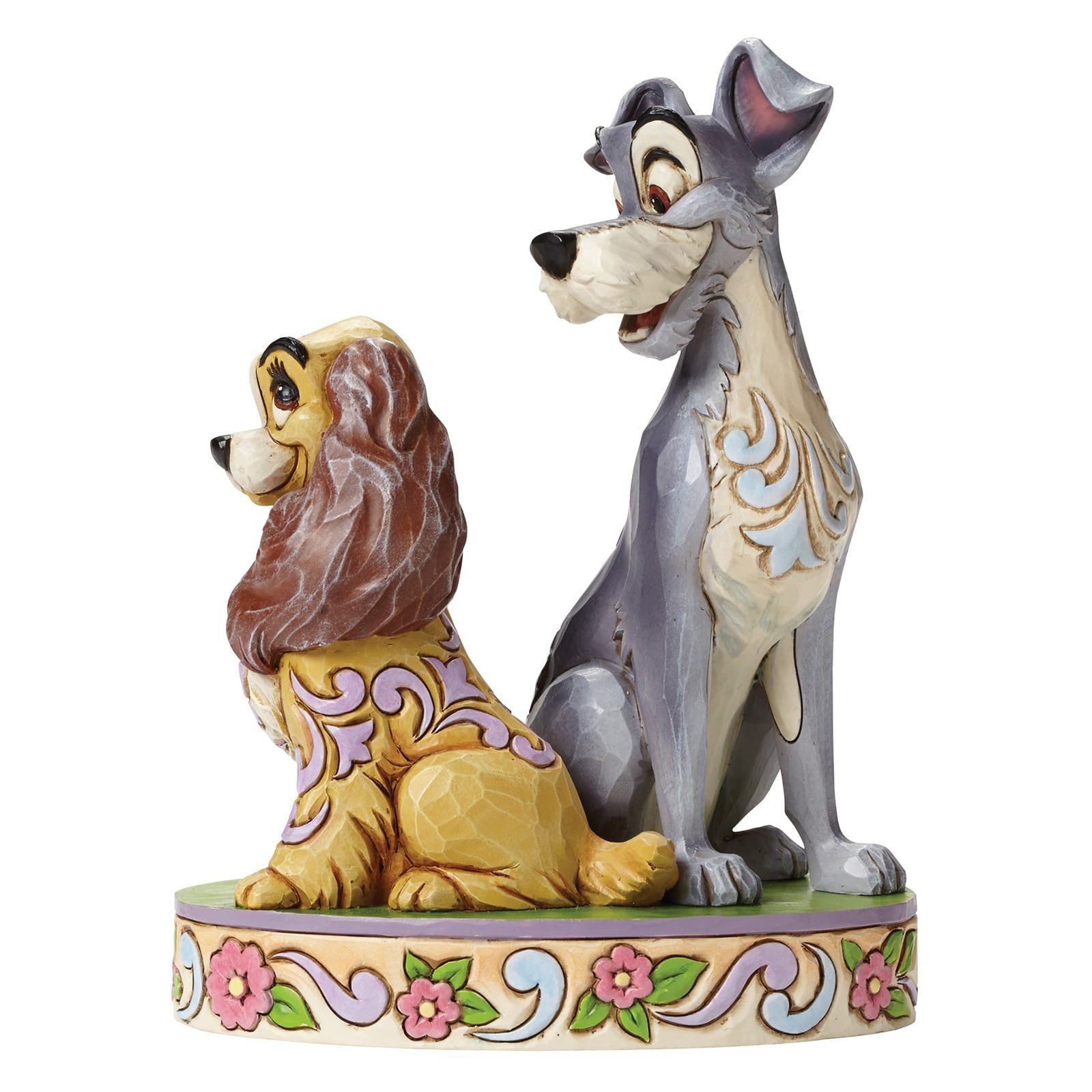 Beeldje van Lady en Tramp, in lichte kleuren, die elkaar aankijken. Decoratieve sokkel met bloemen.