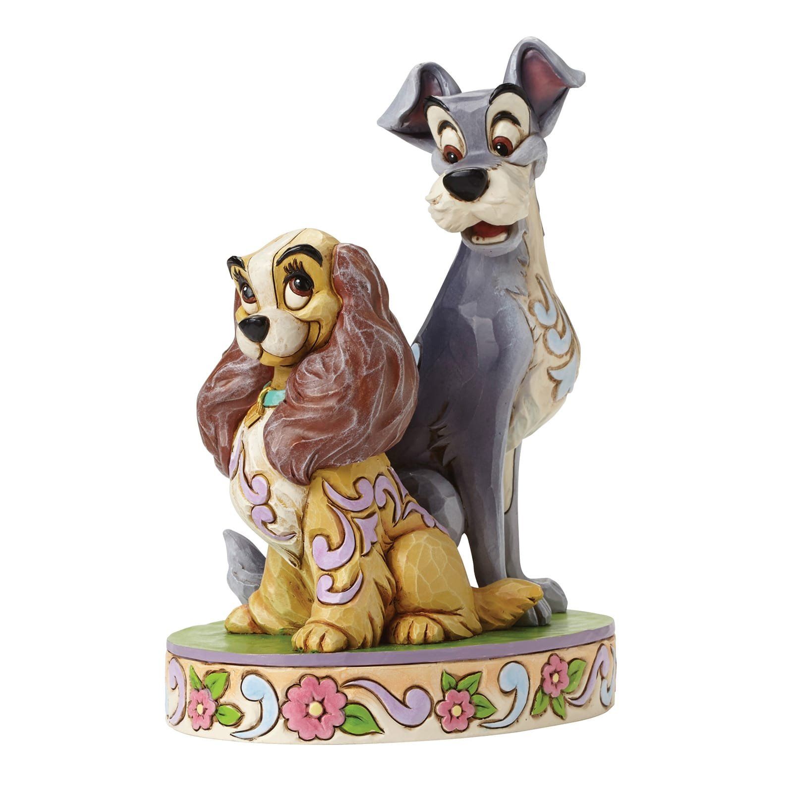 Beeldje van Lady en Tramp, een beige en een grijze hond, op een voetstuk met bloemen.
