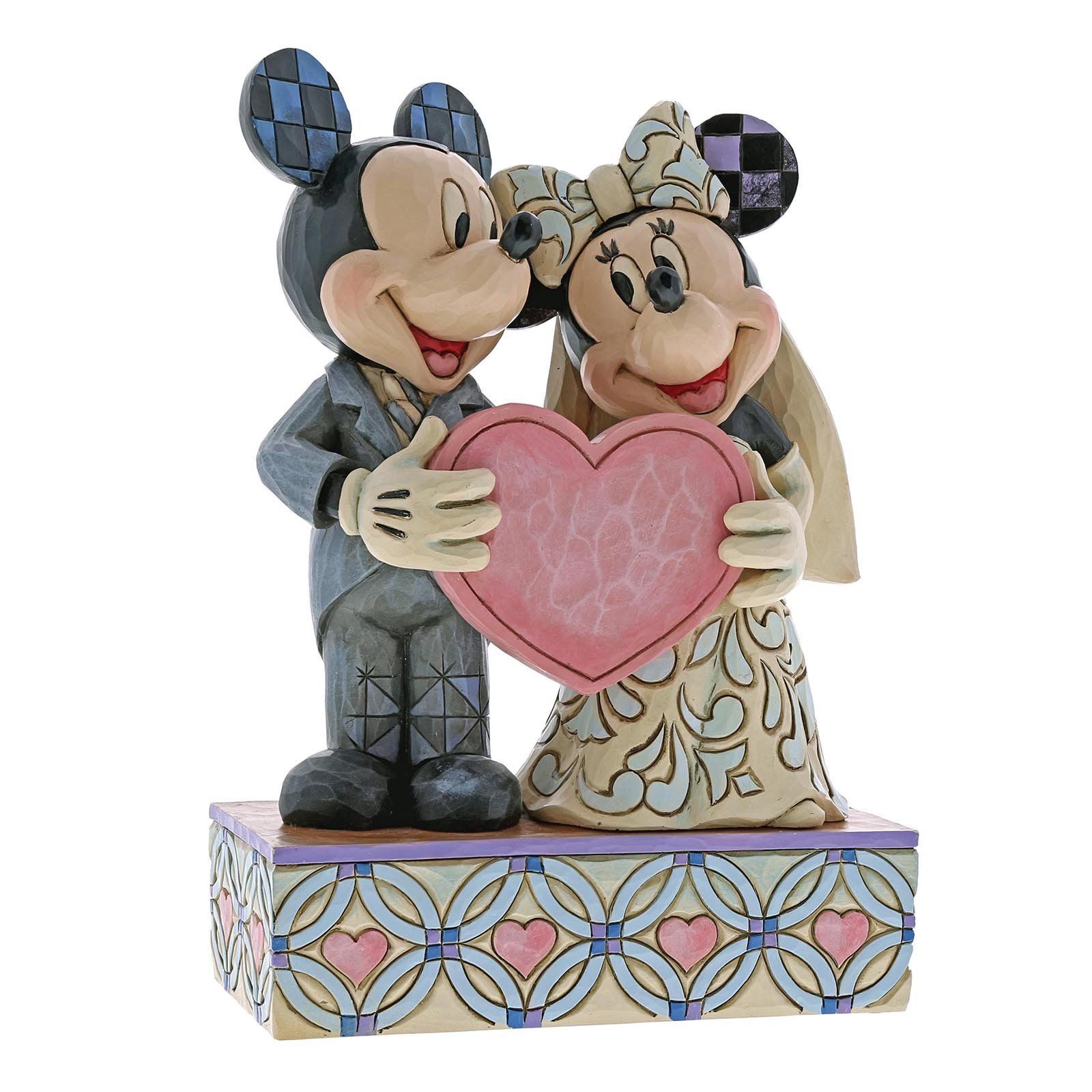 Een beeldje van Mickey en Minnie Mouse die trouwen en een roze hartje vasthouden. Decoratieve voet met dambordpatroon.