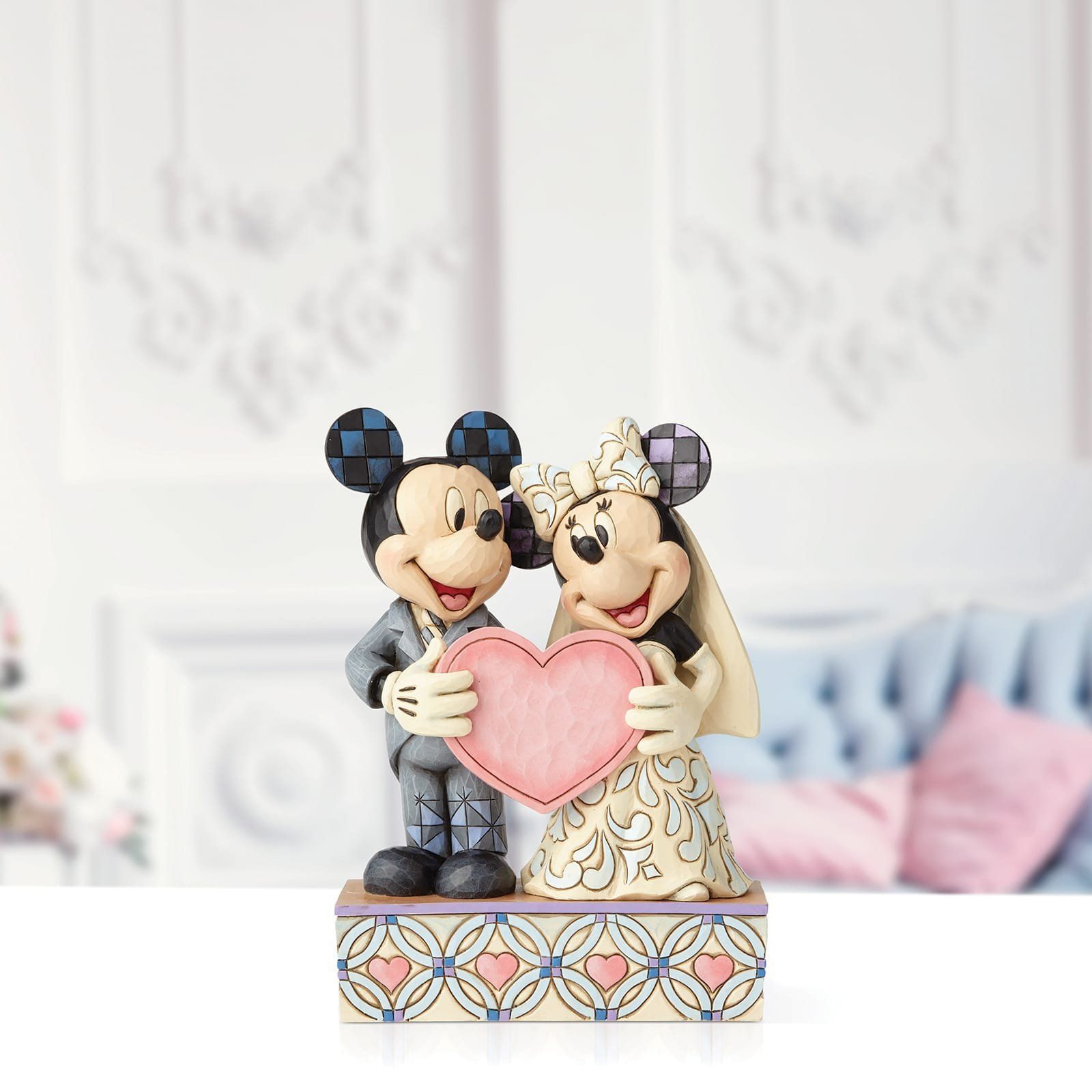 Een beeldje van Mickey en Minnie Mouse die een roze hartje vasthouden. Decoratieve sokkel met hartjes.