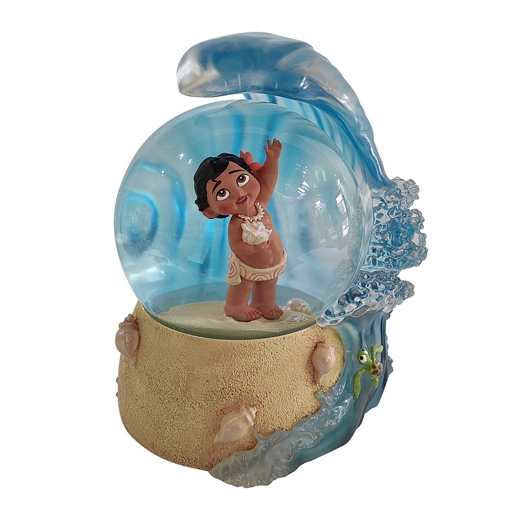 Sneeuwbol met baby Moana, met haar armen omhoog, in een golf, op een zanderige ondergrond met schelpen.