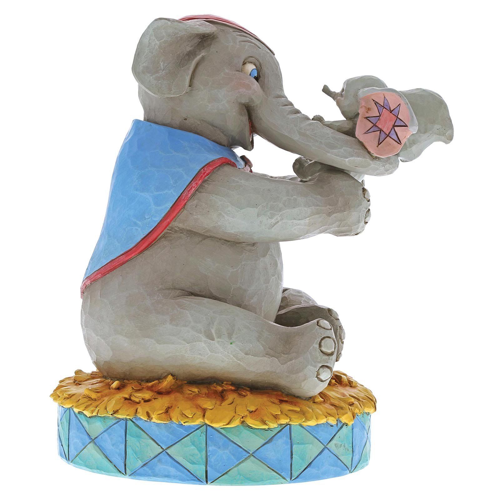 Een zittend grijs olifantenbeeldje met een blauwe cape, dat een babyolifantje vasthoudt en op een circusvoetstuk staat.