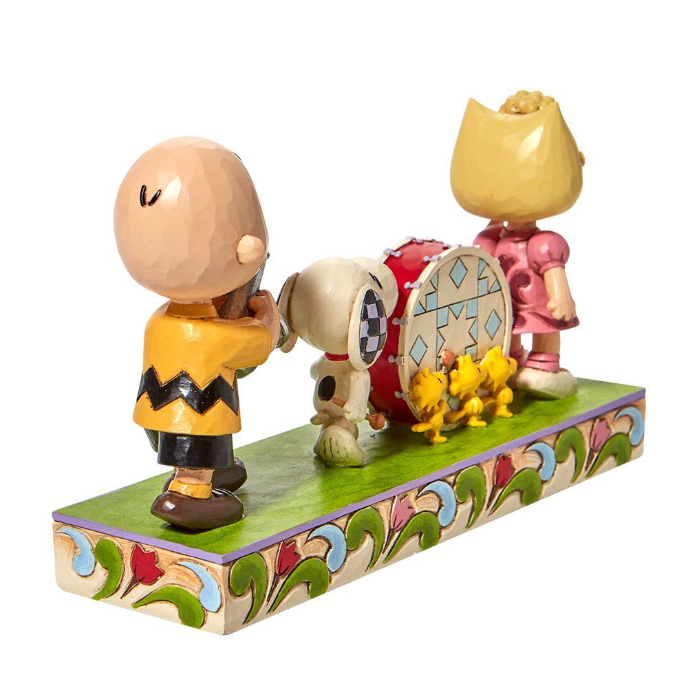 Parade van Peanuts-personages: Charlie Brown, Snoopy, Sally en kuikens op een versierd podium.