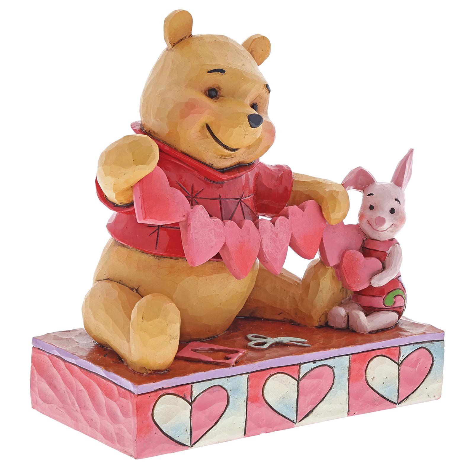 Winnie de Poeh en Knorretje maken een hartjesslinger, zittend op een blok met hartjesmotieven.
