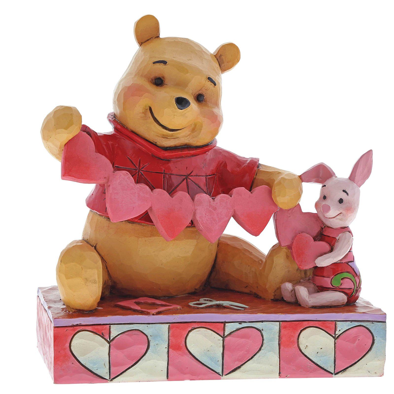 Winnie de Poeh en Knorretje houden een hartjeskrans vast en glimlachen. Rood shirt, roze hartjes, kleurrijke ondergrond.