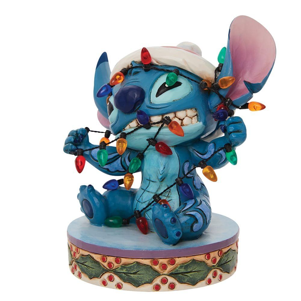 Een Stitch-figuurtje, verstrikt in kerstverlichting, met een hoedje op, zittend op een versierde sokkel.