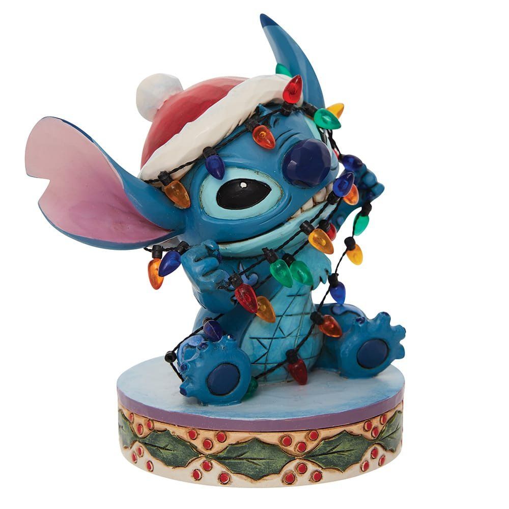 Stitch, met een kerstmuts op en verstrikt in kleurrijke kerstlichtjes, zit op een versierde sokkel.