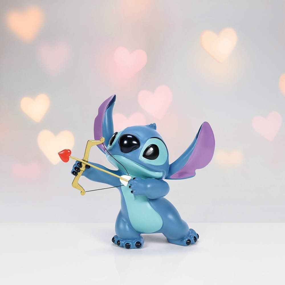 Een Stitch-figuurtje met een gouden boog en een rode hartvormige pijl, met een bokeh-achtergrond in de vorm van een hart.