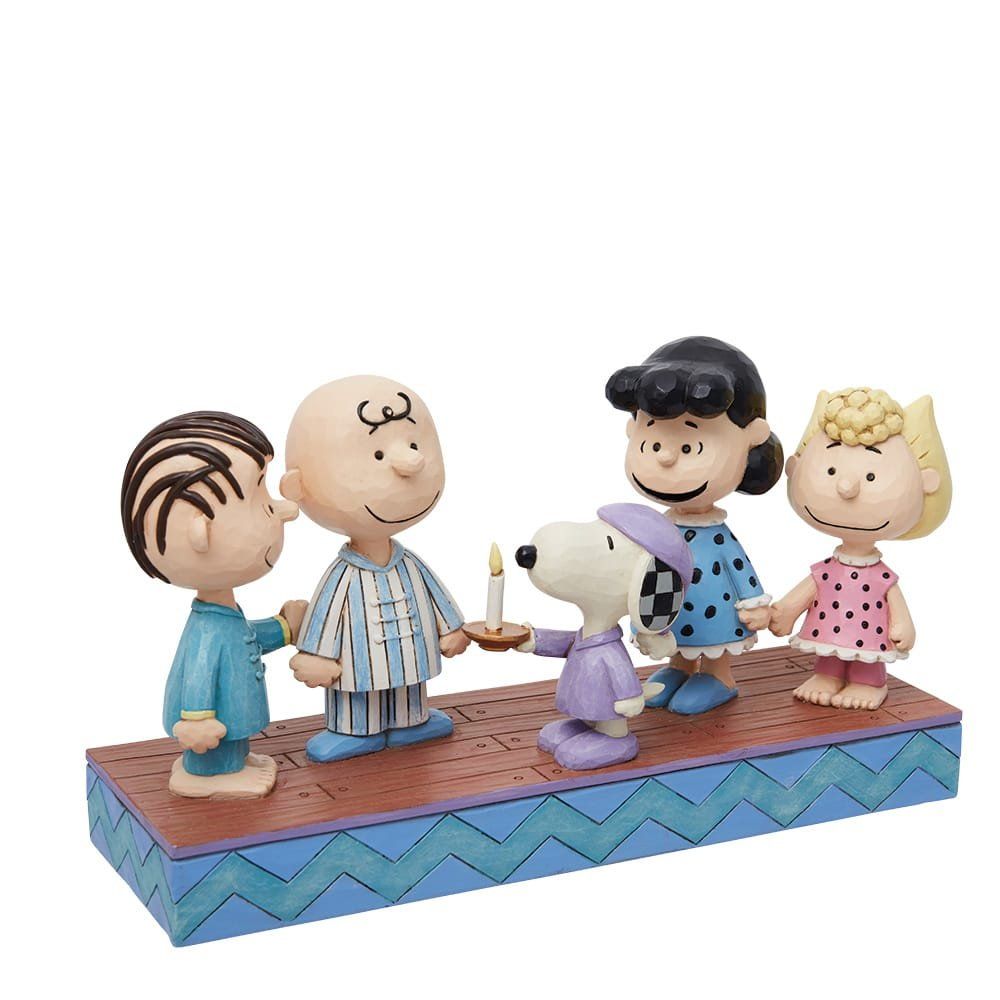 De Peanuts-figuren in pyjama's houden elkaars hand vast, Snoopy met een kaars op een blauw platform.