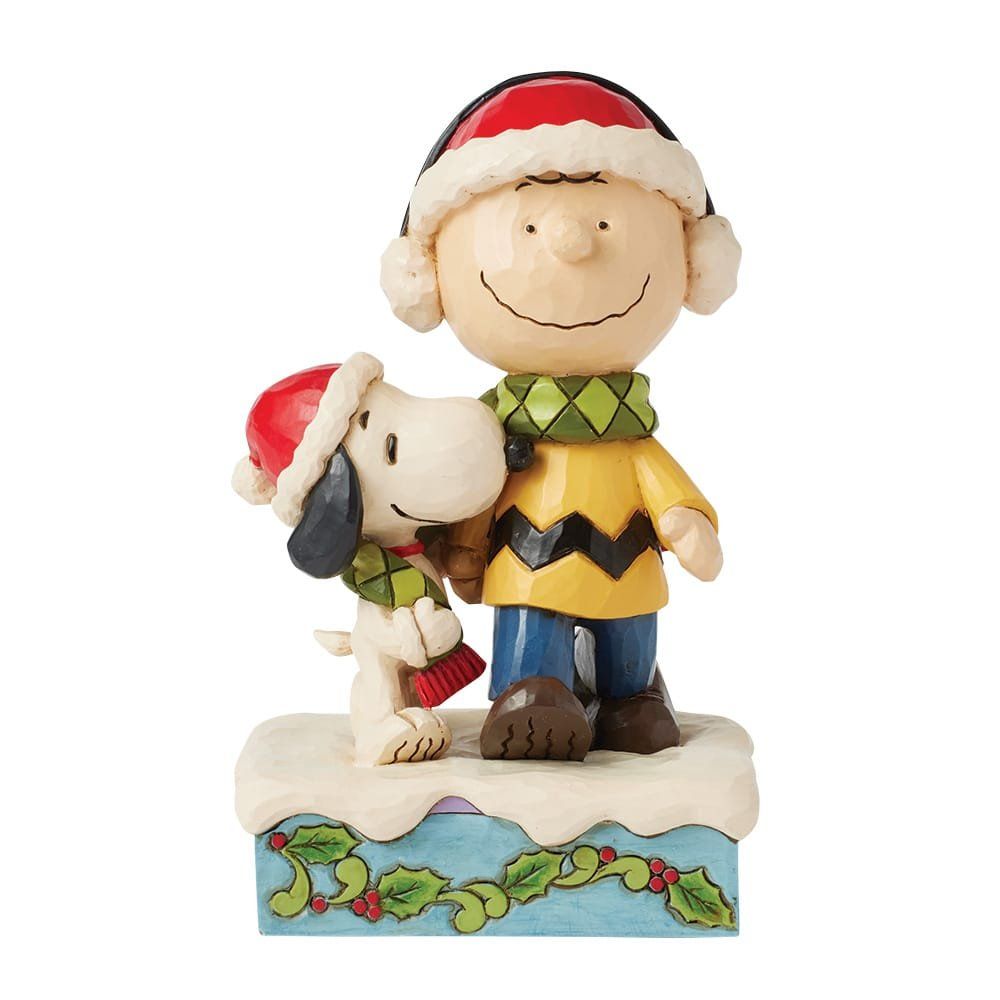 Een kerstfiguurtje van Charlie Brown en Snoopy, met rode mutsen en sjaals, staand op een besneeuwde sokkel.