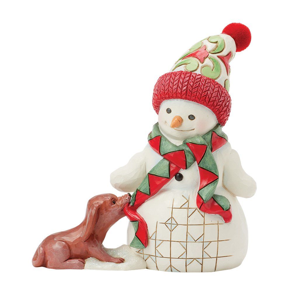Een sneeuwpop met een rode muts, een sjaal en een bruine hond die aan de sjaal trekt.
