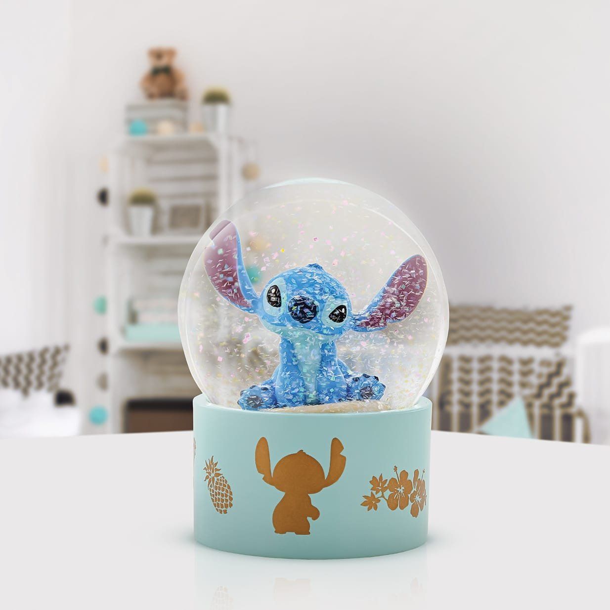 Een sneeuwbol van Stitch met een blauwe voet en gouden accenten, tegen een wazige achtergrond.