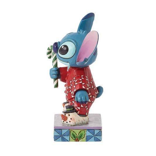 Een Stitch-figuurtje in een rode kerstpyjama met een zuurstok in zijn hand, staand op een sokkel versierd met een sneeuwpop.