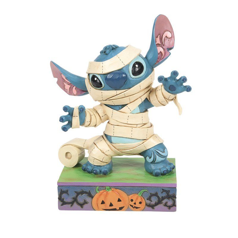 Een Stitch-figuur verkleed als mummie met pompoenen op een sokkel met Halloween-thema.