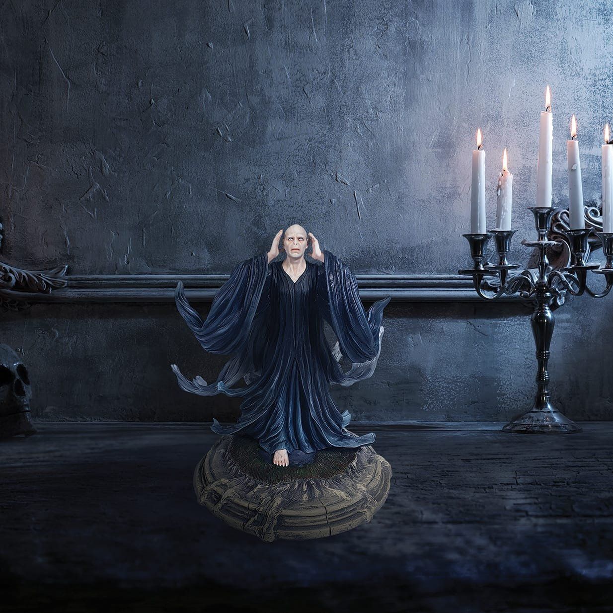 Beeldje van Heer Voldemort, kaal, met opgeheven armen, gekleed in zwarte gewaden, op een stenen sokkel.