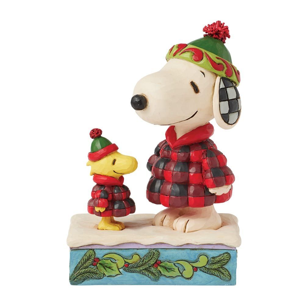 Snoopy- en Woodstock-beeldjes in winterjassen en -mutsen op een besneeuwde ondergrond, afgewerkt met hulsttakken.